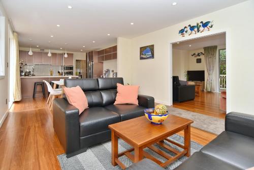 a living room with a black leather couch and a table at Clyde 106 - Christchurch Holiday Homes in Christchurch