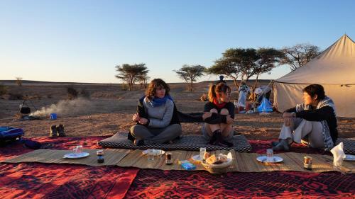 three women sitting on a blanket in front of a tent at jardin du desert in Mhamid