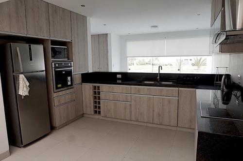 cocina con armarios de madera y nevera de acero inoxidable en Casa 18 en Nuevo Paracas, Condominio Privado, en Paracas