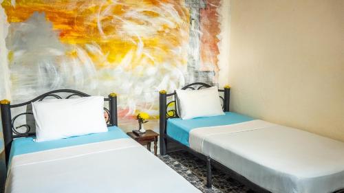 two beds in a room with a painting on the wall at Sabina Guesthouse in Kamala Beach