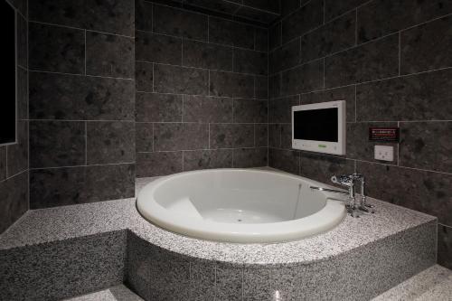 a bathroom with a tub with a tv on the wall at HOTEL Birthday 楠店 in Toyoyama