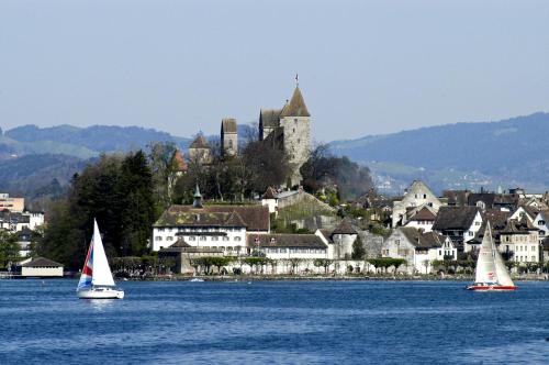 three sailboats in the water in front of a castle at Sorell Hotel Speer in Rapperswil-Jona