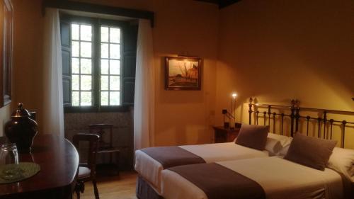 a bedroom with two beds and a table and a window at Pazo da Merced in Neda