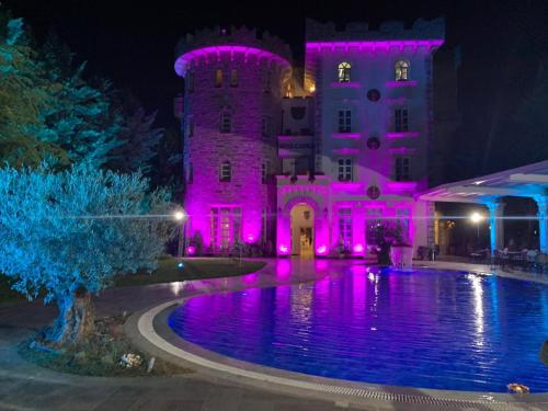 un château éclairé avec des lumières roses en face d'une piscine dans l'établissement Castle Konti, à Tirana