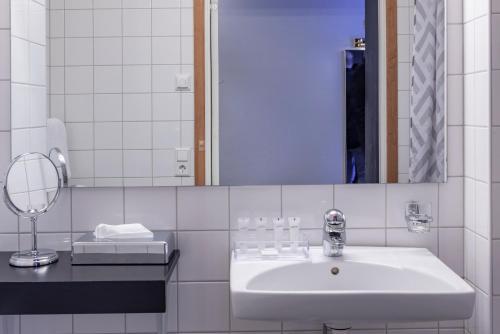 a white bathroom with a sink and a mirror at First Hotel Stadt in Härnösand