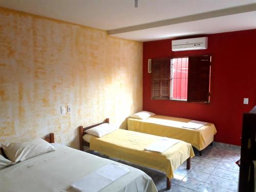 a room with three beds and a red wall at Pousada Bromélias - Suítes e Aptos in Nova Viçosa