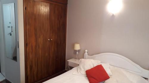 1 dormitorio con cama blanca y almohada roja en el Departamento a media cuadra del mar Edificio "Mont Blanc" en Villa Gesell