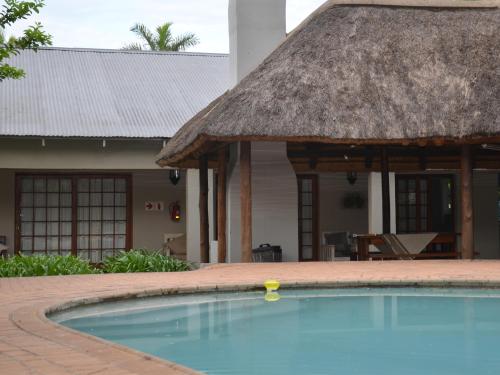 a swimming pool in front of a house with a thatch roof at Stoep Cafe Guest House in Komatipoort