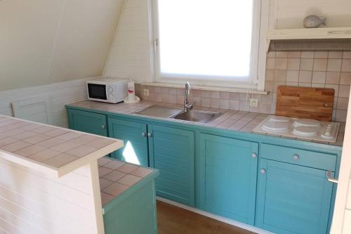 een keuken met blauwe kasten, een wastafel en een raam bij Gezellige chalet in Nieuwpoort - Opkuis al inbegrepen in de prijs in Oostduinkerke