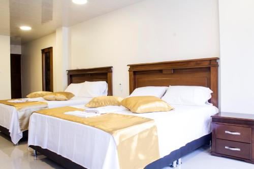 a bedroom with two beds with white sheets and gold pillows at APARTAHOTEL LION in Tuluá