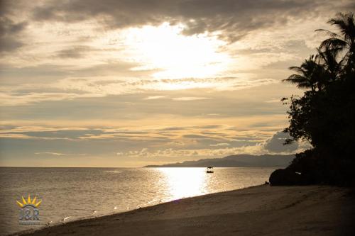 a sunset on a beach with a boat in the water at J&R Residence in Anda
