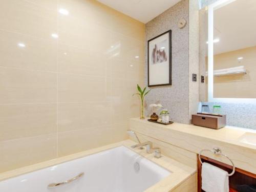 a white bathroom with a tub and a mirror at Binhai Jinling International Hotel in Binhai