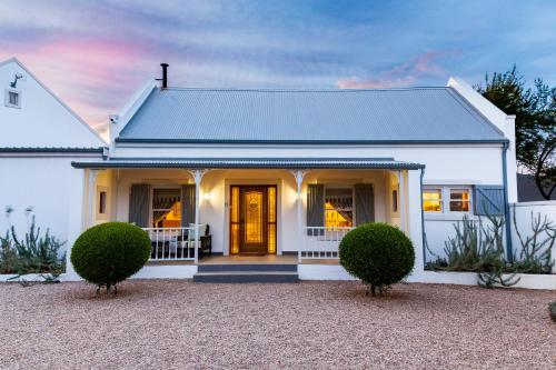 a white house with a yellow door and two bushes at Karoo Masterclass House and Karoo Masterclass Cottage - Accommodation Prince Albert in Prince Albert