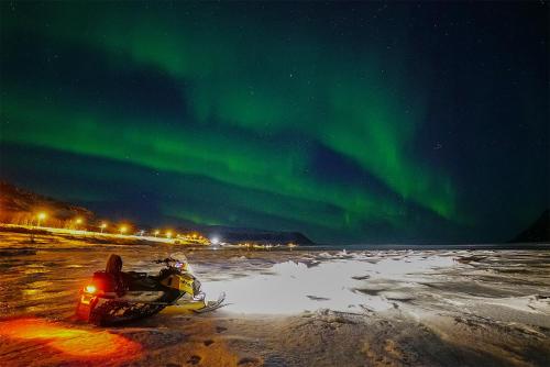 a person riding a snowmobile under the northern lights at Rivdnji Holiday Home Smørfjord in Russenes