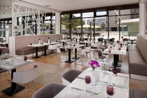 a restaurant with white tables and chairs and windows at INNSiDE by Meliá Wolfsburg in Wolfsburg