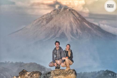 a man and a woman sitting on a rock in front of a mountain at Nachelle Homestay in Berastagi