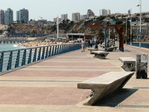 a sidewalk with benches next to the water and a city at La Otra Vista in Valparaíso