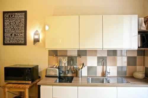 une cuisine avec des armoires blanches, un évier et un micro-ondes dans l'établissement Le 112, confortable et cosy en plein centre d'Aix les Bains, à Aix-les-Bains