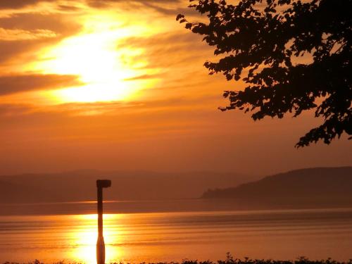 a sunset over the water with a pole in the foreground at La Grange aux Hiboux Gîte et Restaurant B&B in La Baie