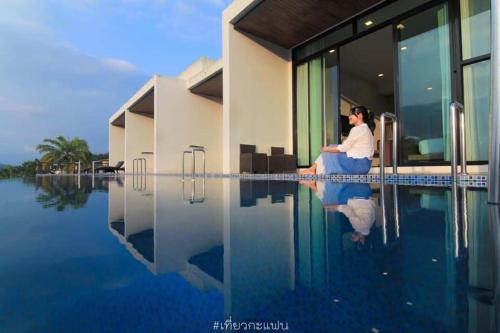 a woman sitting on a chair next to a swimming pool at Belong Jin The Dam Hotel And Resort in Ban Pha Saeng Lang