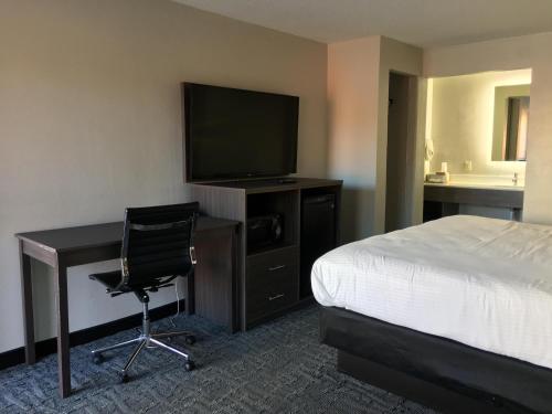 a hotel room with a bed and a desk with a television at Days Inn & Suites by Wyndham Charleston Airport West in Charleston