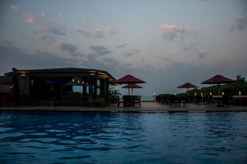 a swimming pool with tables and umbrellas next to the water at Brightland Resort & Spa in Mahabaleshwar