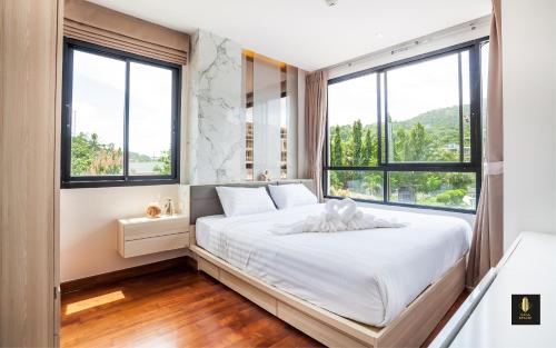 a bedroom with a bed with white sheets and windows at The Lago Naiharn by Sala Estate in Nai Harn Beach