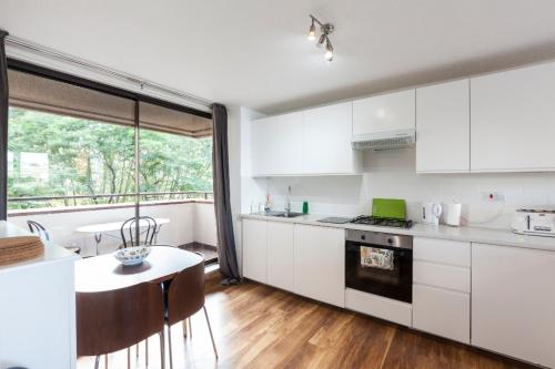倫敦的住宿－泰特現代河景公寓，厨房配有白色橱柜、桌子和窗户。