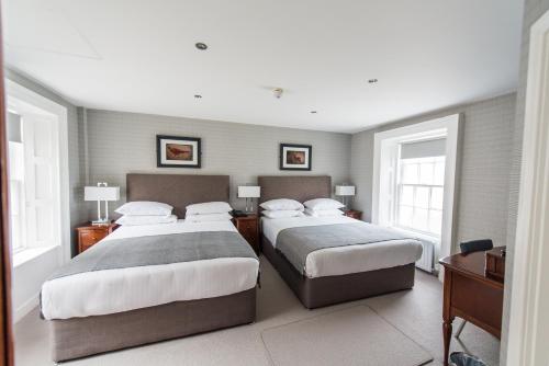 a bedroom with two beds and a desk and two windows at Belmont House Hotel in Banbridge