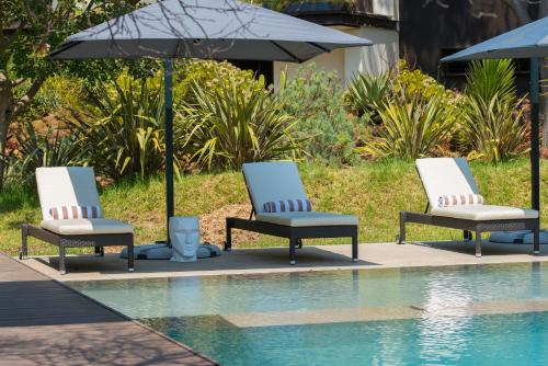 three lounge chairs and an umbrella next to a swimming pool at Vivari Hotel and Spa by Mantis in Johannesburg