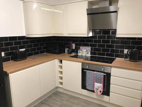 a kitchen with white cabinets and a black tile wall at Webb Lodge in Telford