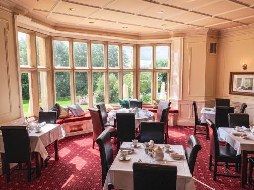 a restaurant with tables and chairs in a room with windows at Hollins Hall Hotel, Golf & Country Club in Bradford