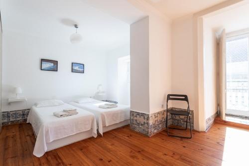 a white bedroom with two beds and a chair at FLH Sé Apartment in Lisbon