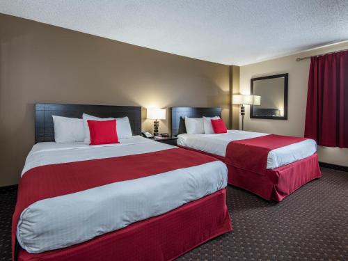 2 łóżka w pokoju hotelowym z czerwonymi poduszkami w obiekcie Paradise Inn & Conference Centre w mieście Grande Prairie