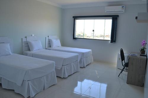 Cette chambre blanche comprend 3 lits et une fenêtre. dans l'établissement Tradicional Plaza Hotel, à Nerópolis