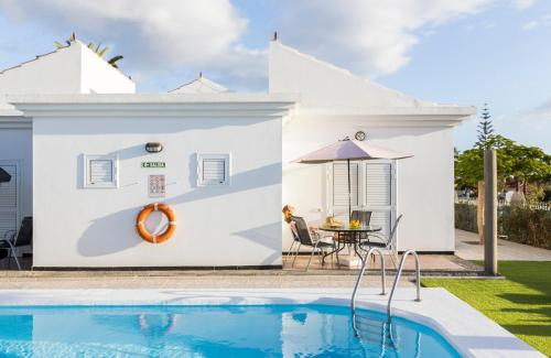 a villa with a swimming pool in front of a house at Bungalows Las Almenas in Maspalomas