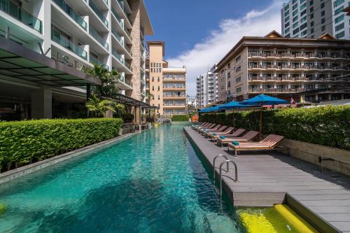a swimming pool with chairs and umbrellas next to buildings at Hotel Vista in Pattaya Central