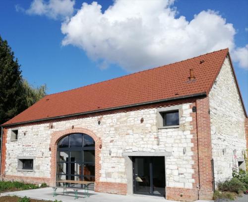 un bâtiment en briques avec un toit rouge dans l'établissement La Grange Du Bosquet, à Honnecourt-sur-lʼEscaut