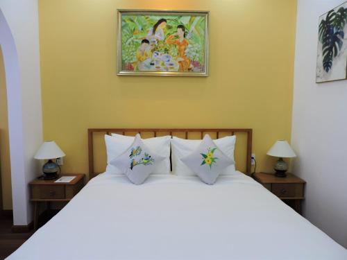 a bedroom with a bed with white pillows and a painting at Chez Mimosa Local in Ho Chi Minh City
