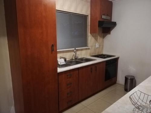 uma cozinha com armários de madeira, um lavatório e uma janela em Rocky Ridge Guest House SELF Catering - No alcohol allowed em Roodepoort