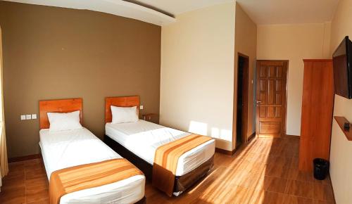 two beds in a hotel room with a television at Bluefire Homestay Syariah in Banyuwangi