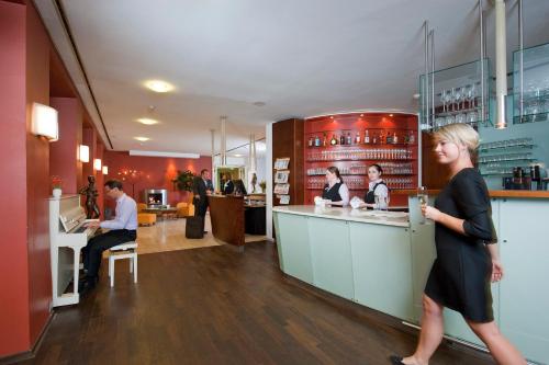 a woman walking past a bar in a restaurant at Parkhotel Wolfsburg in Wolfsburg