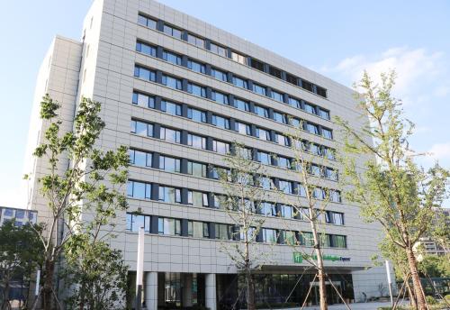 a white building with trees in front of it at Holiday Inn Express Wuxi Taihu New City by IHG in Wuxi