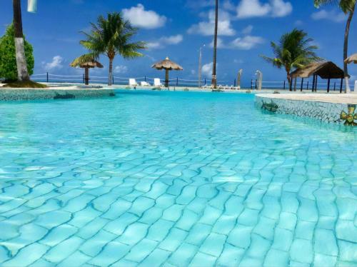 a swimming pool with blue water and palm trees at Village Galés Maragogi - Chalé 03 in Maragogi
