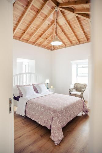 a white bedroom with a large bed and a chair at Villa Mariense in Vila do Porto