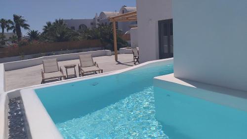 a swimming pool with two chairs next to a house at Filira Suites in Perissa