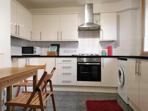 a kitchen with white cabinets and a wooden table and chairs at Cosy Flat Close To East Dulwich Station in London