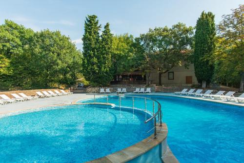 a large swimming pool with white chairs and trees at Hotel PRESLAV in Golden Sands