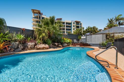 a swimming pool with a resort building in the background at Mylos Holiday Apartments in Alexandra Headland