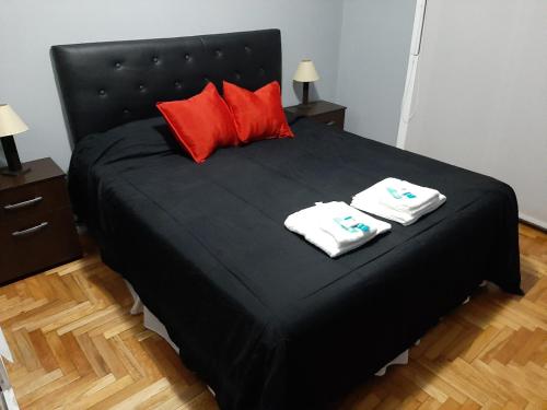 1 cama negra con almohadas rojas y 2 toallas en Caballito Sun en Buenos Aires